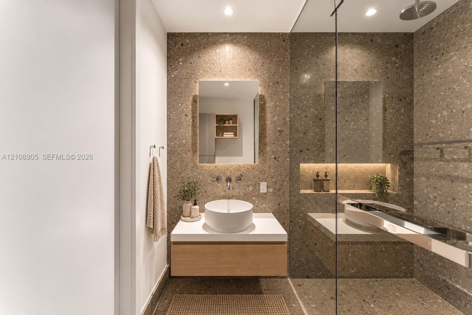 Floating wood-finish vanity with a white vessel sink, wall-mounted faucet, integrated recessed shelving with lighting, and floor-to-ceiling stone-composite wall cladding