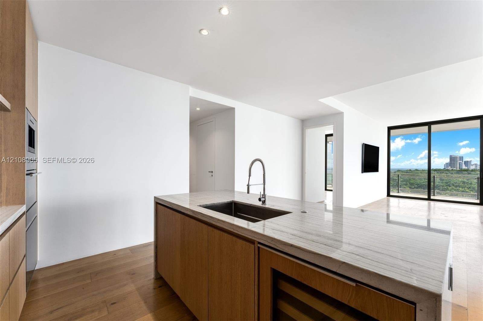 Modern kitchen featuring an island with stone countertops, undermount sink, built-in wine refrigeration, and wood-finish cabinetry