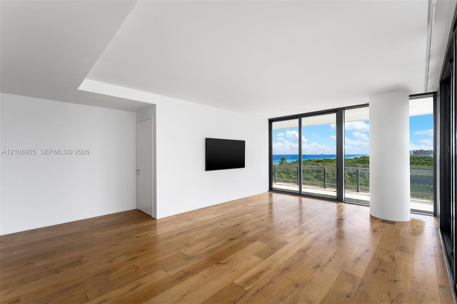 Interior space featuring wood-finish flooring, floor-to-ceiling sliding glass doors, a structural support column, and a balcony with an ocean backdrop