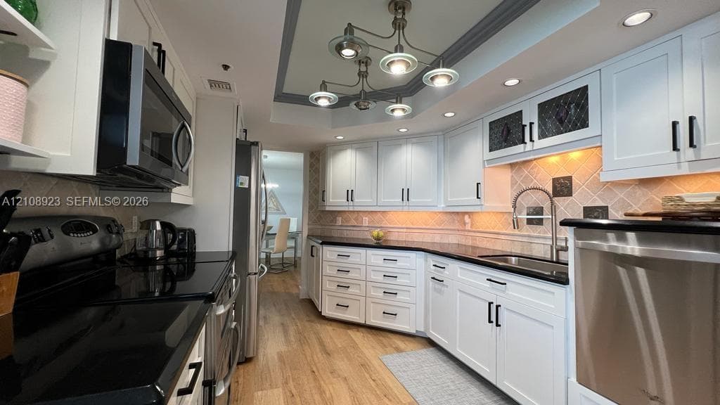 Kitchen featuring white cabinetry, black stone countertops, wood-finish flooring, a multi-arm chandelier, and stainless steel appliances