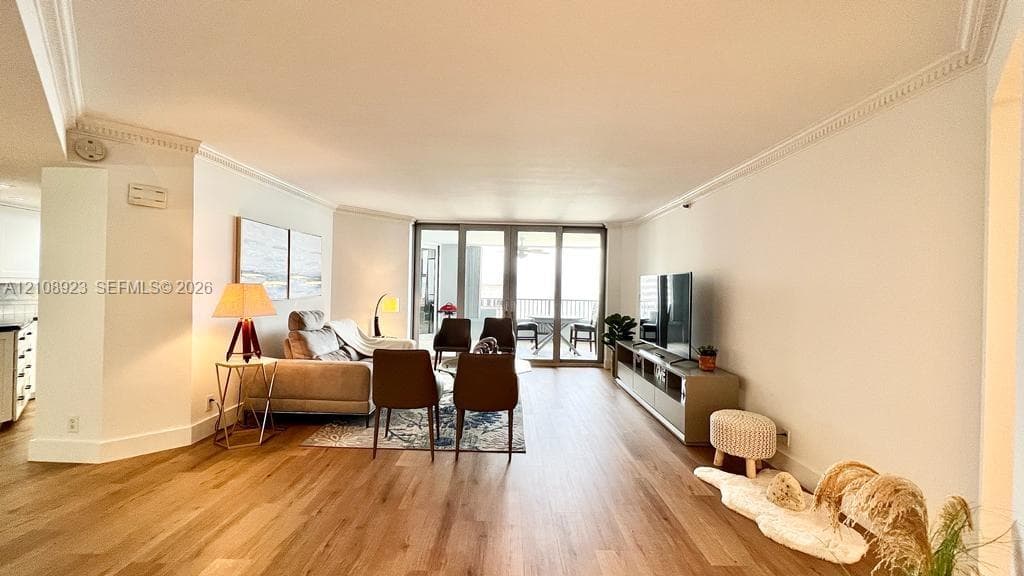 Open-concept room featuring wood-finish flooring, crown molding, and large sliding glass doors providing outdoor access