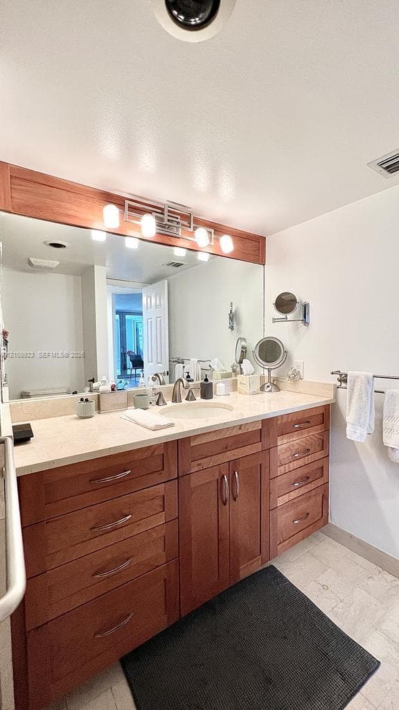 Wood-finish vanity cabinetry with multiple storage drawers, light-toned countertop featuring an integrated sink, expansive mirror, and a wall-mounted multi-bulb light fixture