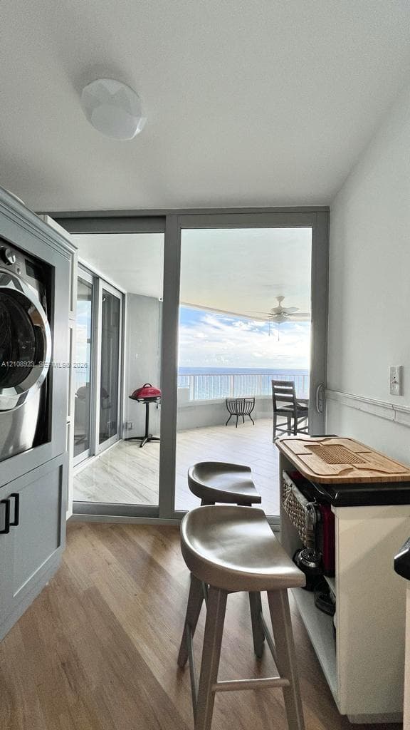Built-in cabinetry with integrated laundry appliances, wood-finish flooring, and expansive floor-to-ceiling glass sliding doors opening to an outdoor balcony