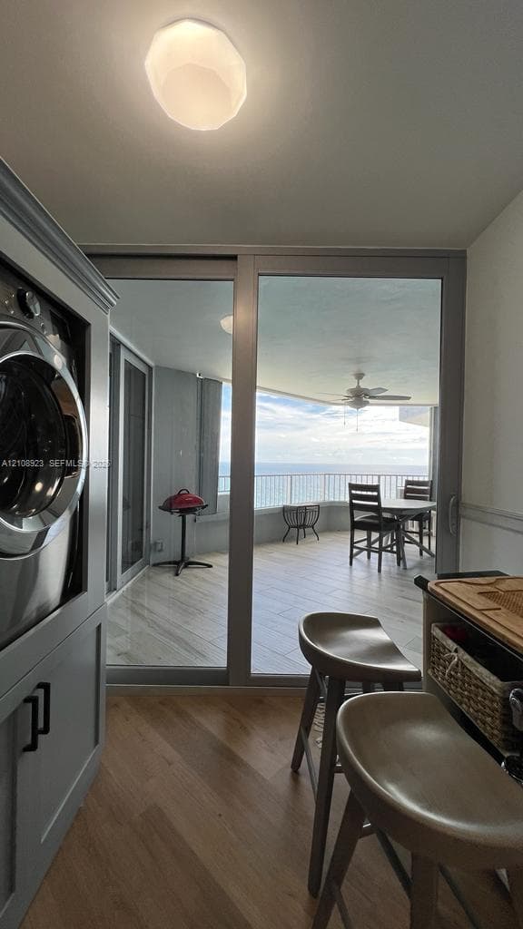 Built-in laundry cabinetry with integrated washer, wood-finish flooring, floor-to-ceiling sliding glass doors, and expansive covered balcony with tile flooring