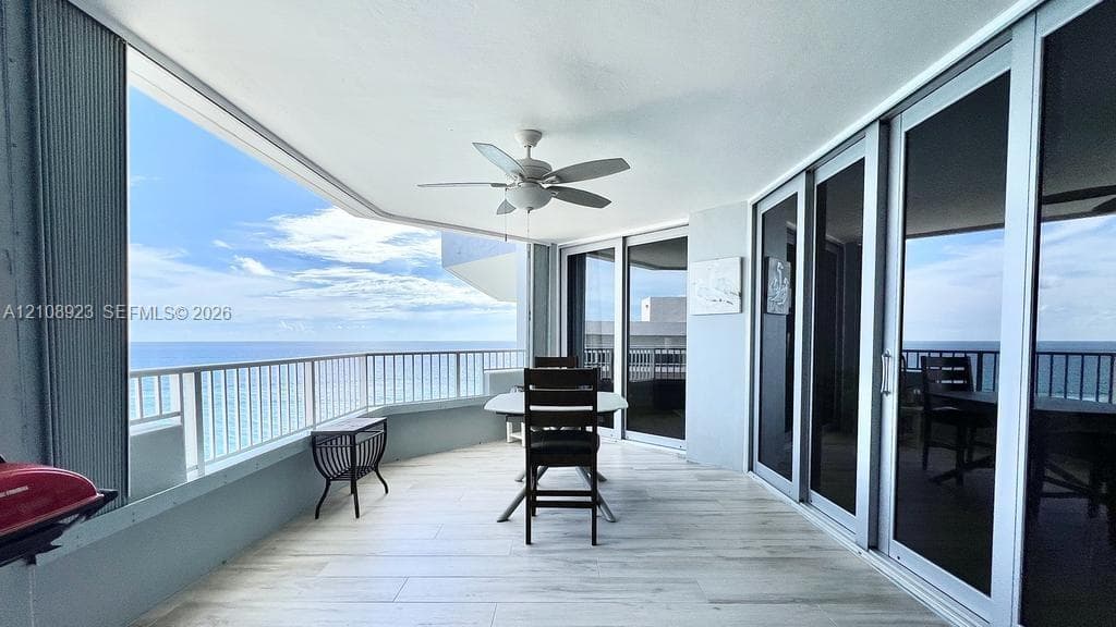 Covered balcony featuring wood-finish tile flooring, white metal railings, a ceiling fan, and multi-panel sliding glass doors