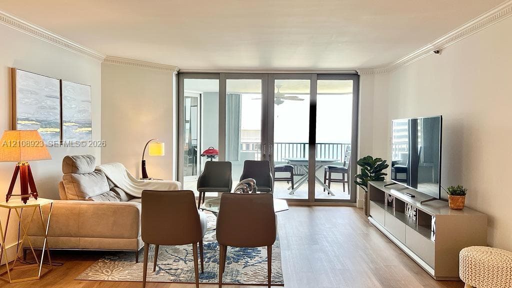 Living area featuring wood-finish flooring, crown molding, and floor-to-ceiling glass panel doors leading to a balcony