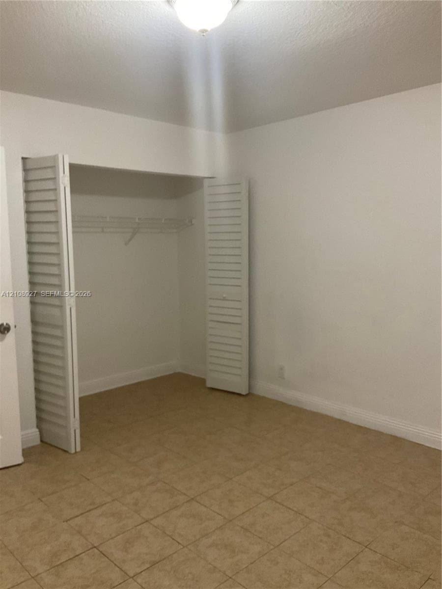 Room featuring tile flooring, a closet with white louvered bi-fold doors, and a ceiling-mounted light fixture