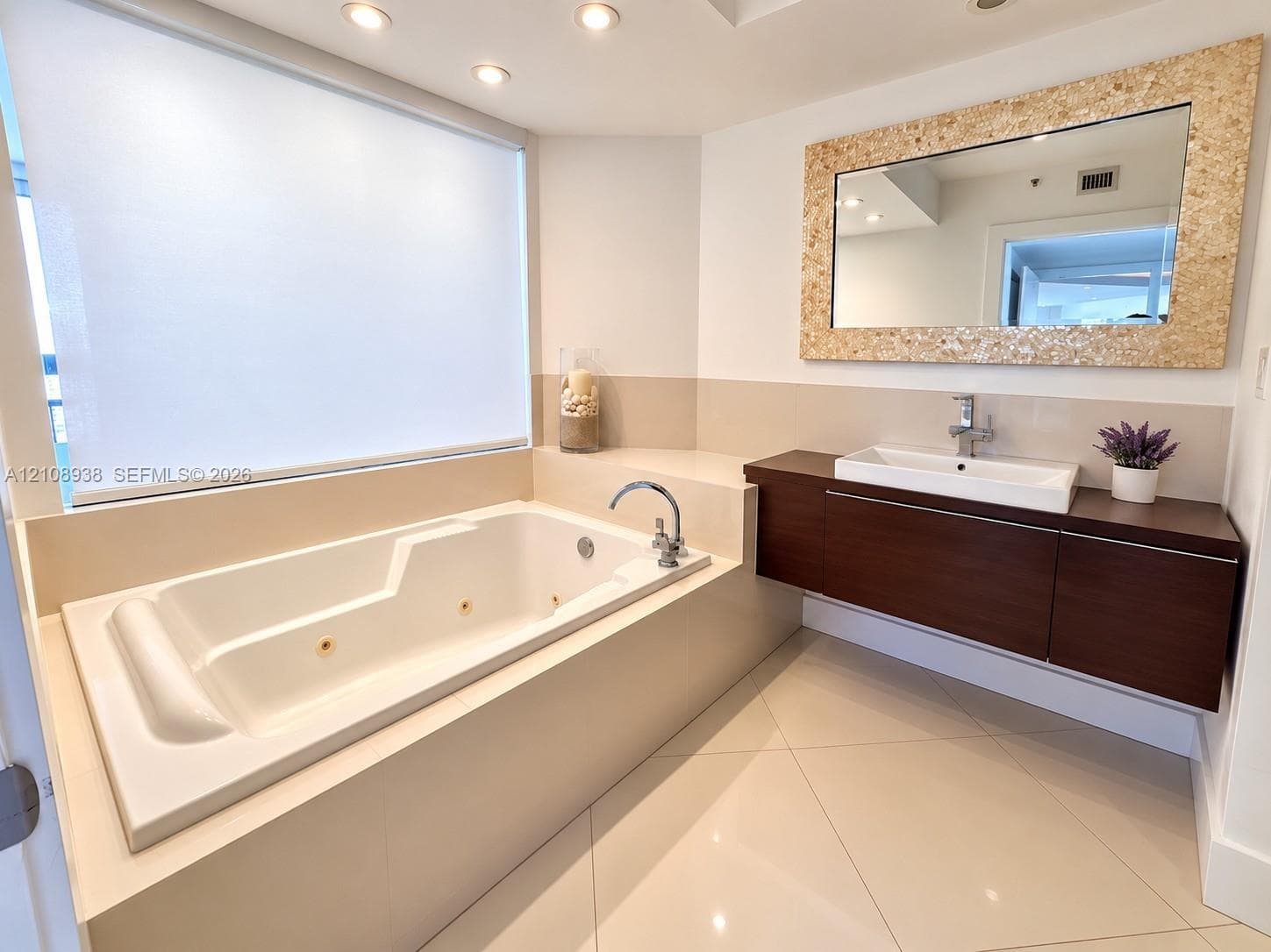 Bathroom featuring a jetted soaking tub, floating vanity with a rectangular vessel sink, large-format tile flooring, recessed ceiling lighting, and a decorative framed mirror