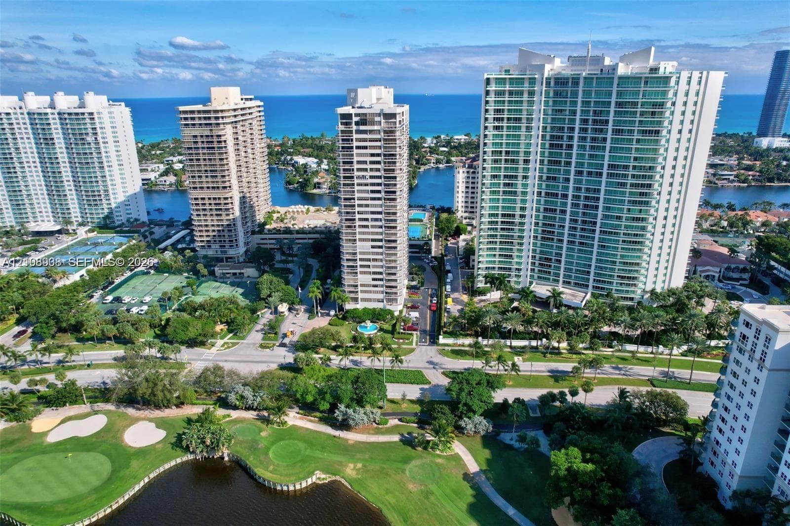Aerial perspective featuring high-rise architecture, proximity to the coastline, and surrounding golf course grounds