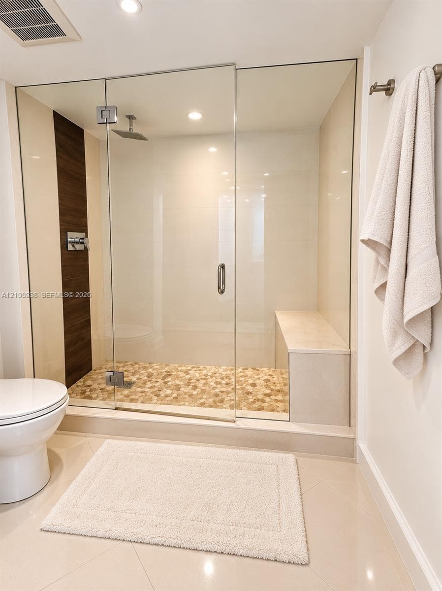 Walk-in shower featuring a frameless glass enclosure, pebble-stone flooring, integrated built-in bench, rain-style showerhead, and dark wood-tone vertical wall accent