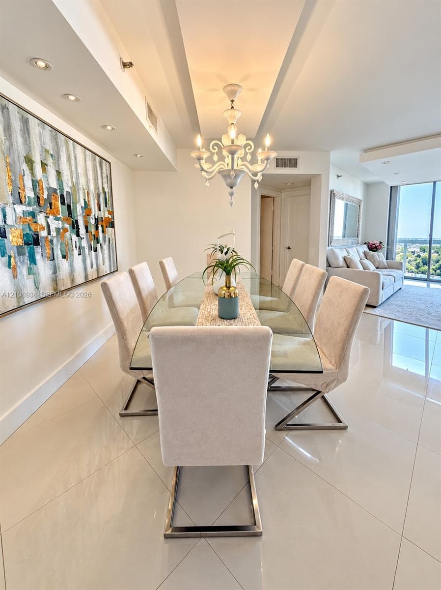 Dining area featuring polished large-format tile flooring, a decorative tiered chandelier, recessed accent lighting, and a recessed ceiling design