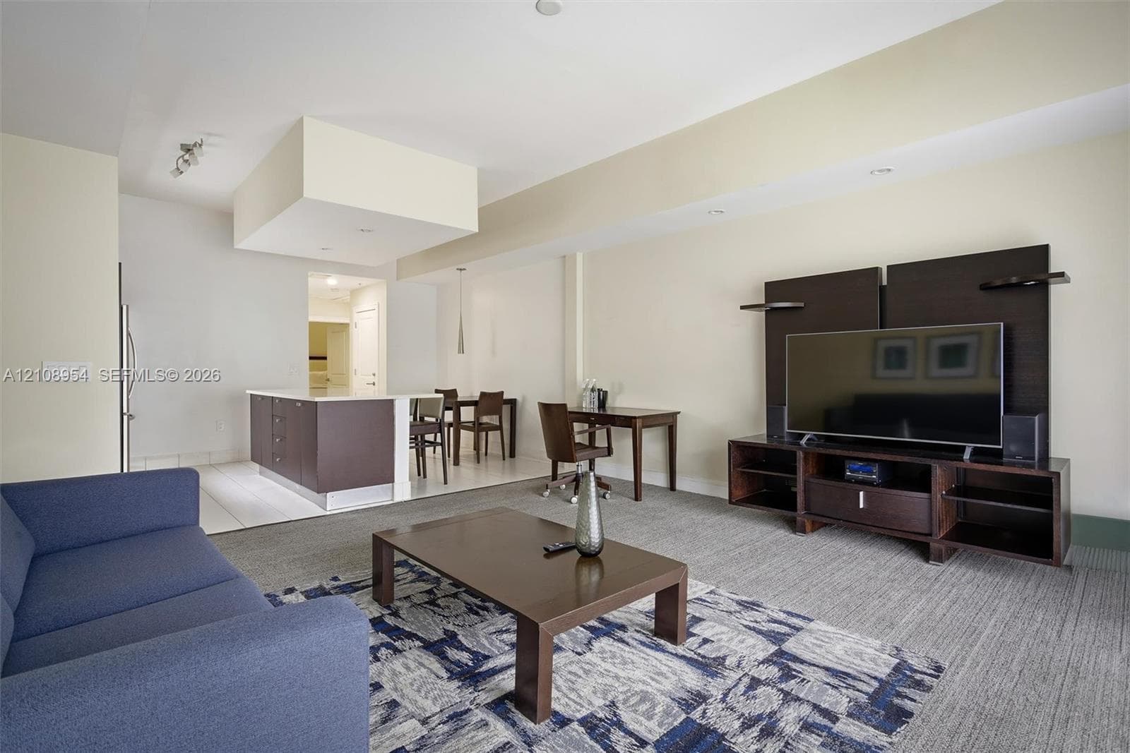 Open-concept floor plan featuring a kitchen island with dark cabinetry, recessed lighting, and wall-to-wall carpeting