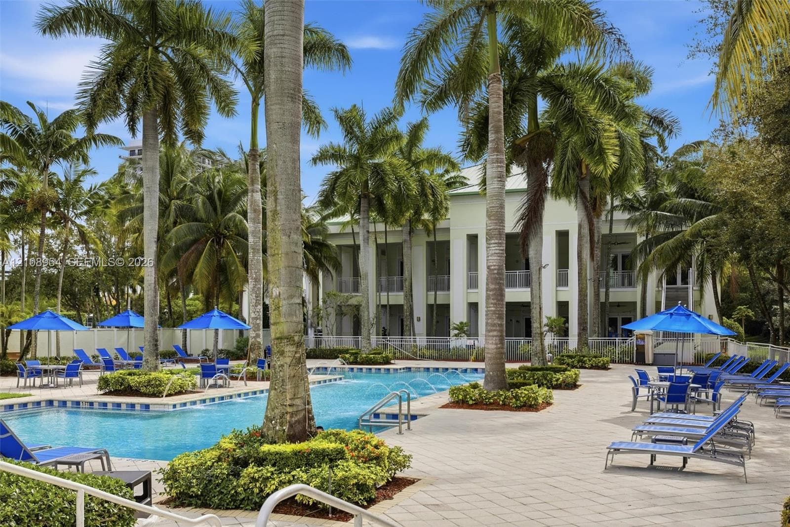 Swimming pool featuring water jets and a paved surround, complemented by mature palm trees and manicured landscaping