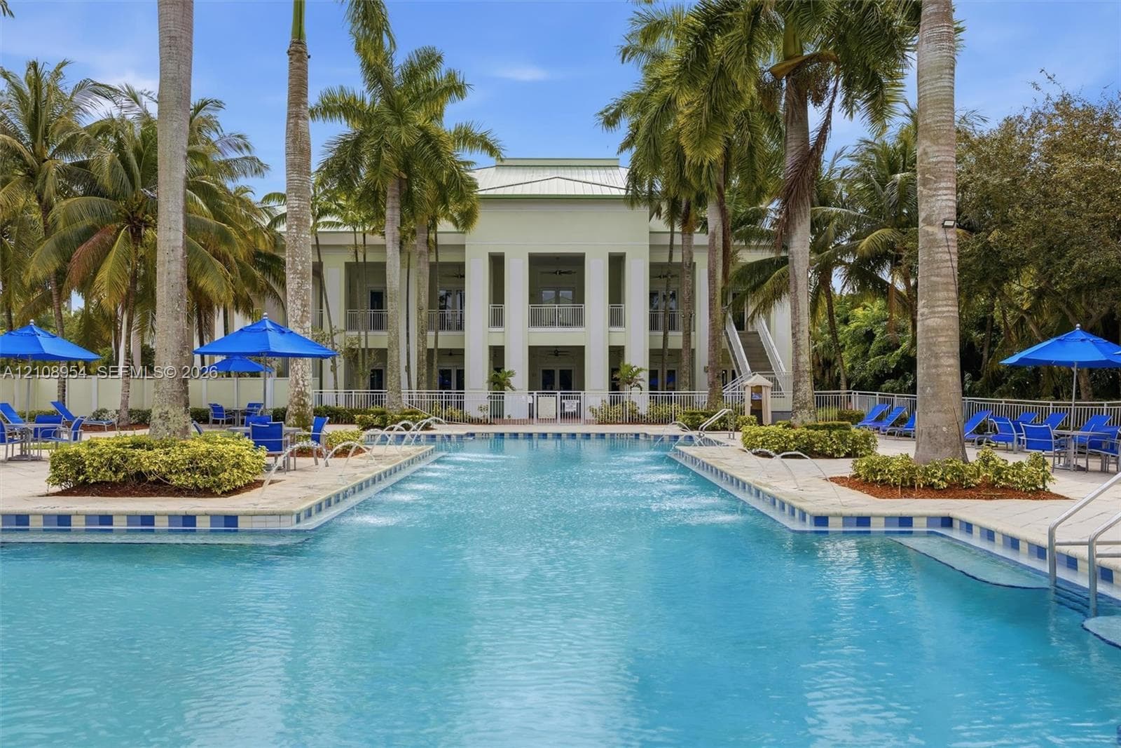 Resort-style pool featuring integrated water jets, a tile-accented perimeter, stone-finish decking, and mature palm landscaping