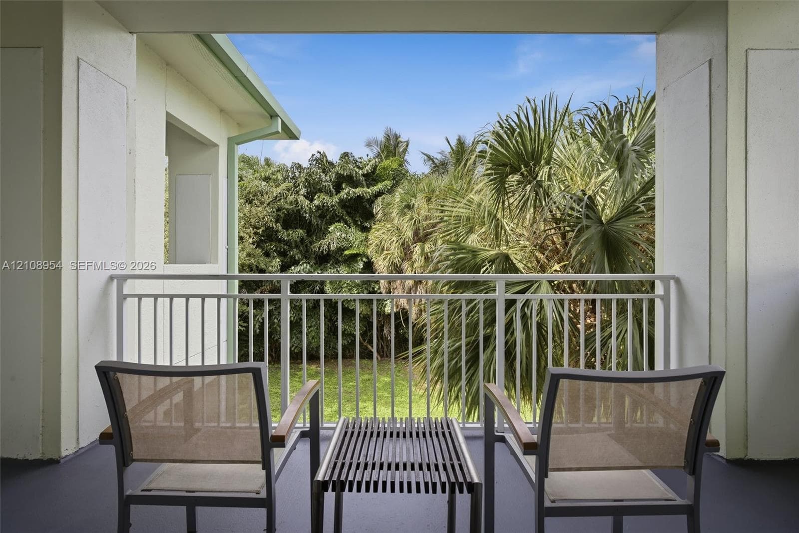 Covered balcony featuring white metal railings and greenery backdrop