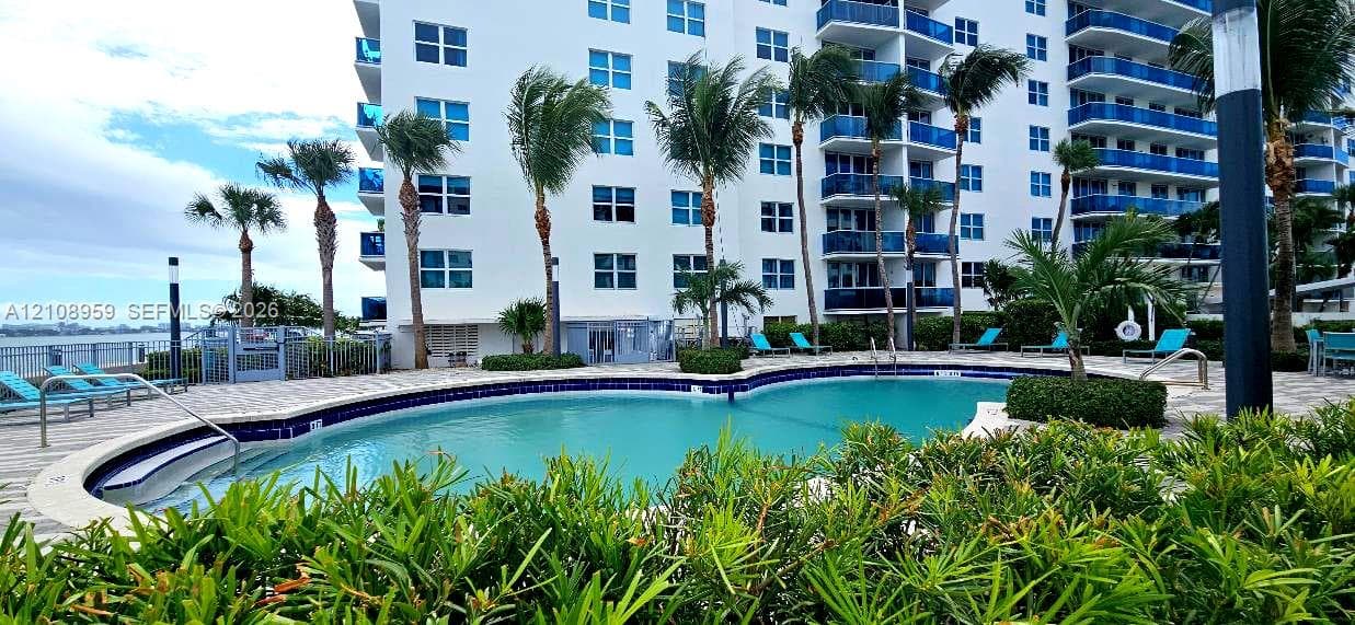 Resort-style pool featuring stone-paver decking, mature palm landscaping, and metal perimeter fencing