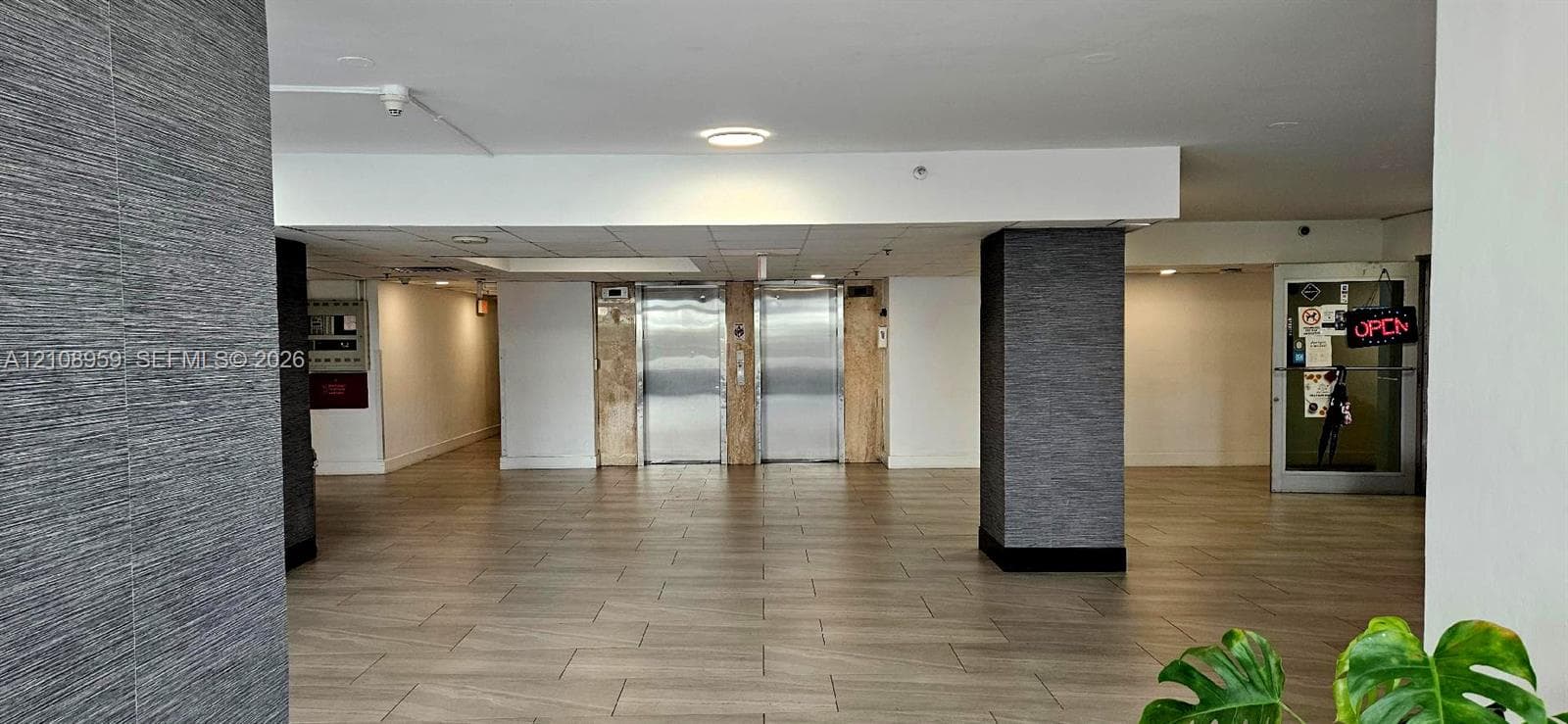 Lobby area featuring wood-finish flooring, dual stainless steel elevators, and textured charcoal wall cladding