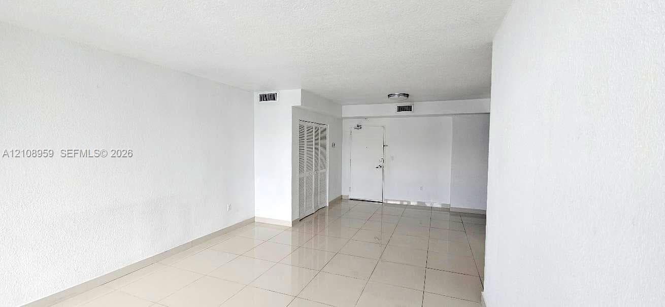 Open-concept interior featuring light-toned tile flooring, textured wall finishes, and white louvered closet doors