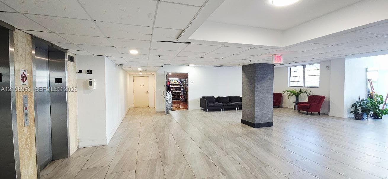 Lobby area featuring large-format tile flooring, recessed lighting, brushed metal elevator doors, and a central architectural pillar with textured finish
