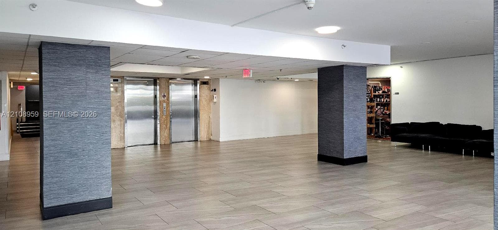 Lobby featuring large-format tile flooring, textured grey column cladding, and dual stainless steel elevator doors