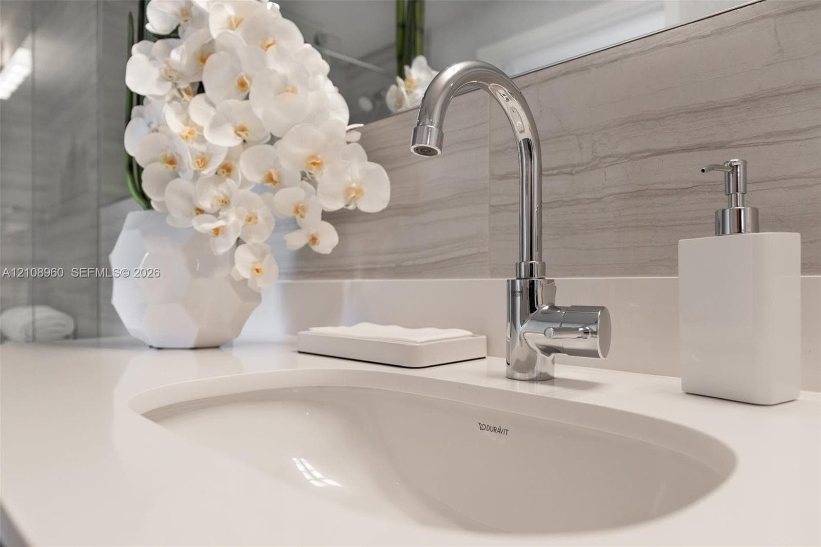 Undermount oval sink with a polished chrome faucet and solid-surface countertop, complemented by horizontal-veined stone wall tile and a full-width mirror