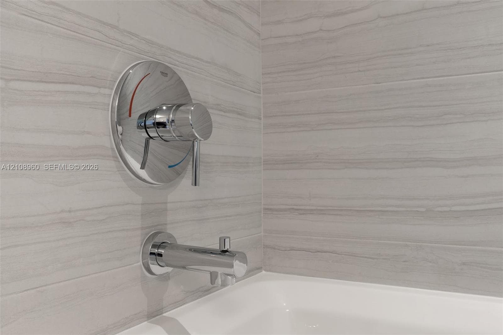 Linear-patterned stone tile surround, polished chrome single-handle faucet, integrated tub spout, and white porcelain bathtub