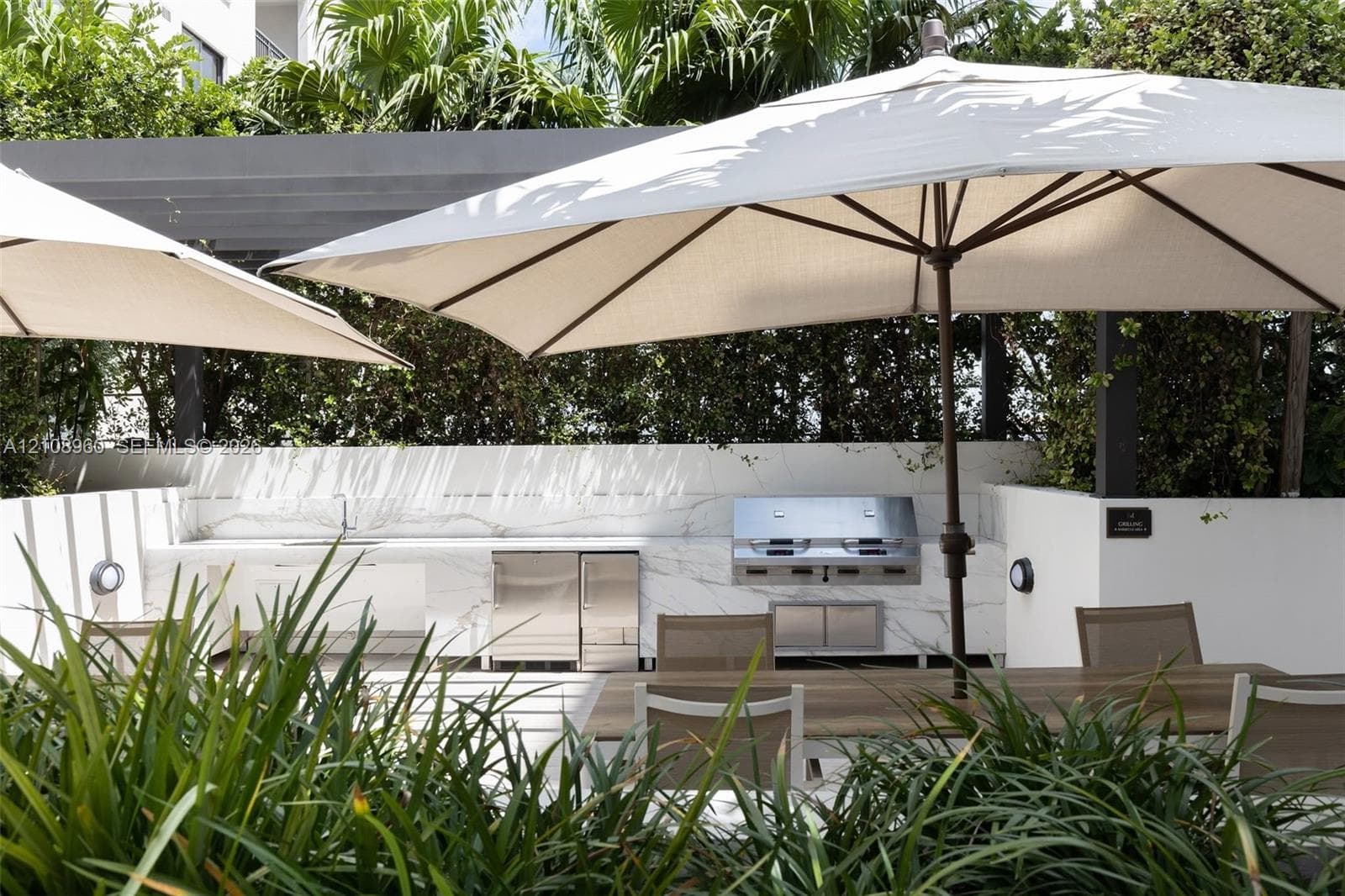 Outdoor kitchen featuring stone-surface countertops, built-in stainless steel grill, stainless steel under-counter refrigerator, sink, and overhead pergola structure