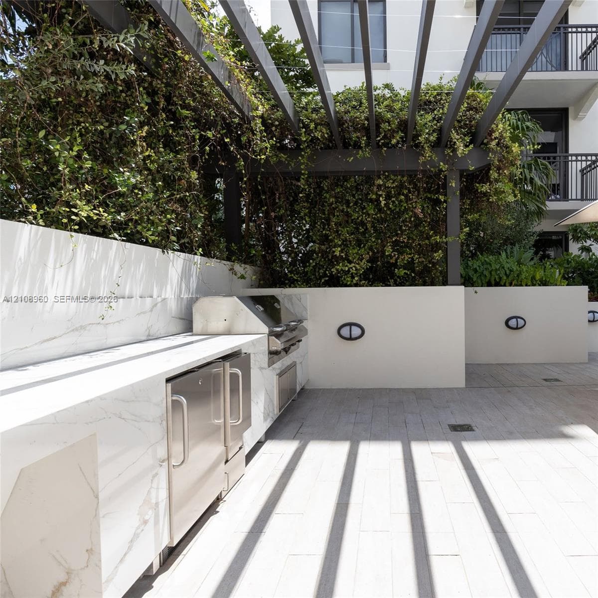 Outdoor kitchen featuring stone-finish counters, integrated stainless steel appliances, a pergola, and paver flooring