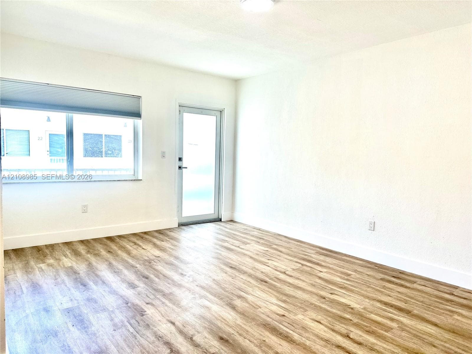 Interior space featuring wood-finish flooring, white walls, a large single-pane window, and a glass-paneled exterior door