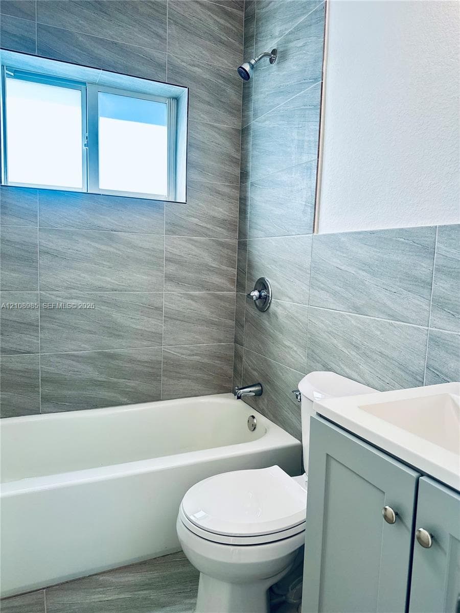 Bathroom featuring gray wall-to-wall ceramic tile, a white soaking tub with metallic hardware, and a vanity cabinet with a integrated countertop sink