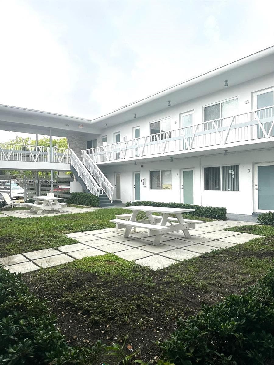 Exterior courtyard featuring a central lawn, concrete paver sections, white metal railings, and dual-level exterior walkways