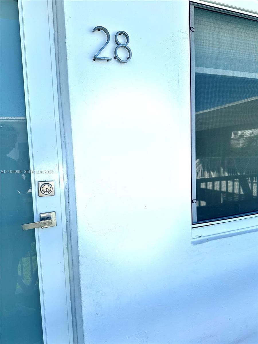 Smooth white stucco exterior featuring a modern brushed-metal address numeral, a frosted glass pane entry door, and a rectangular window with a thin-profile frame