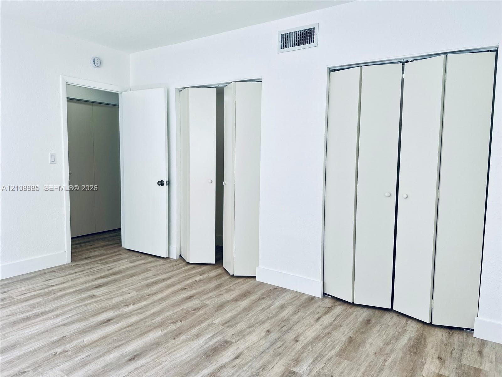 Neutral-toned wood-finish flooring, two sets of white bi-fold closet doors, and a solid-core interior swing door