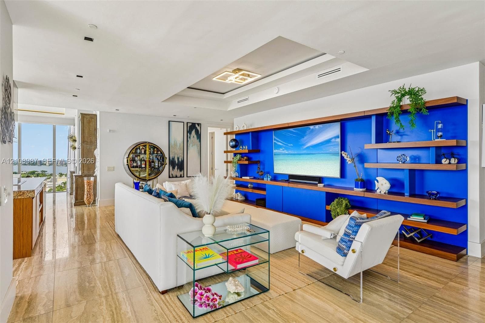Living space featuring polished stone flooring, custom built-in shelving with integrated lighting, a recessed tray ceiling, and floor-to-ceiling windows