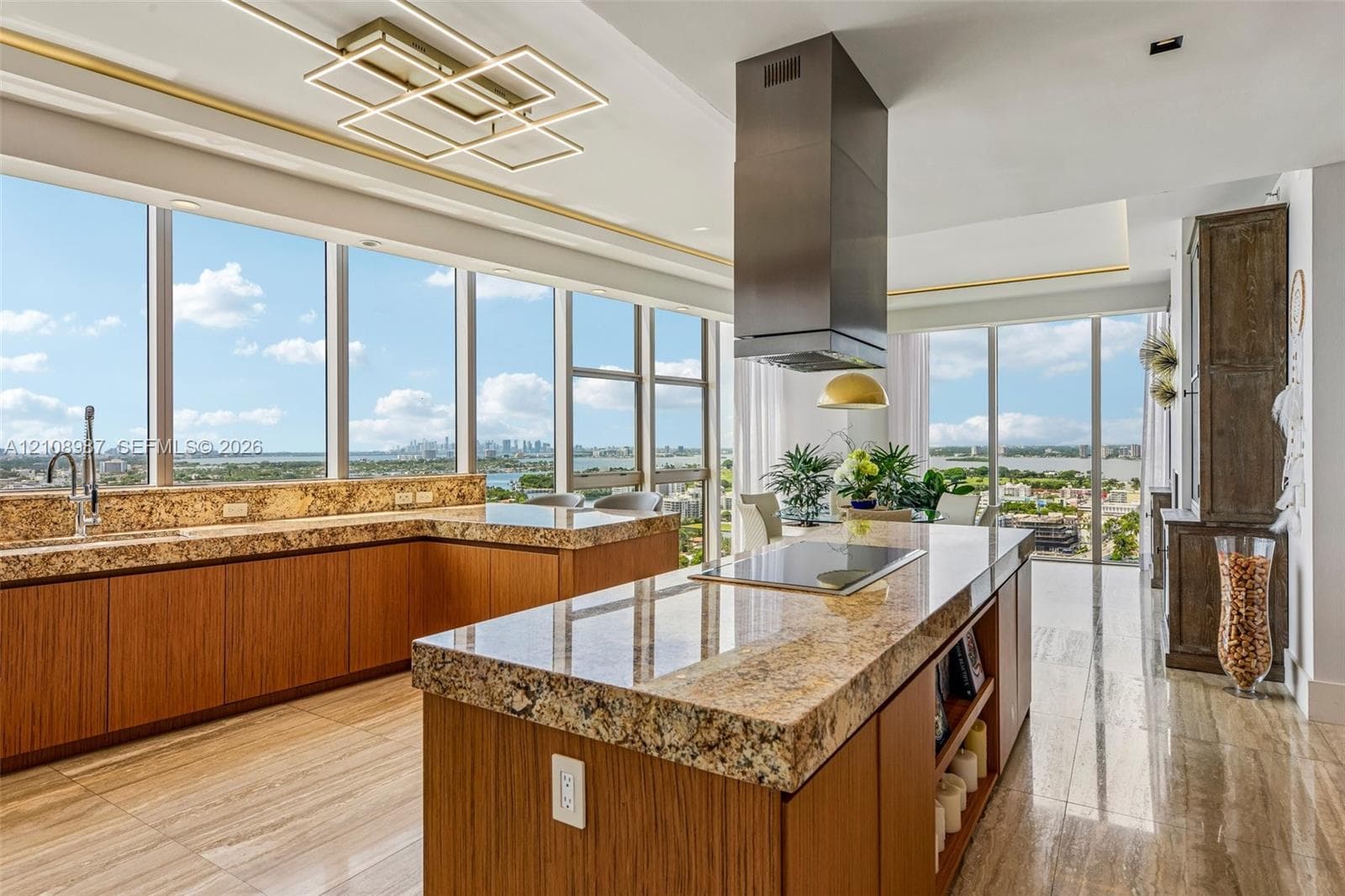 Kitchen featuring extensive stone countertops, custom wood-finish cabinetry, floor-to-ceiling glass windows, stainless steel range hood, and large-format tile flooring