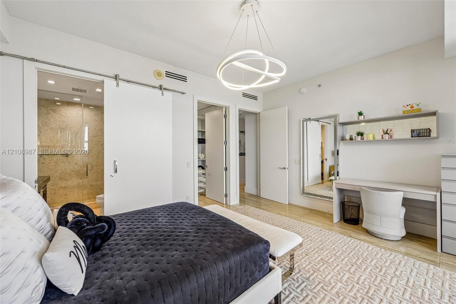 Contemporary architectural space featuring a stainless steel sliding barn door, minimalist circular LED pendant lighting, built-in wall-mounted desk with integrated shelving, and neutral wood-finish flooring