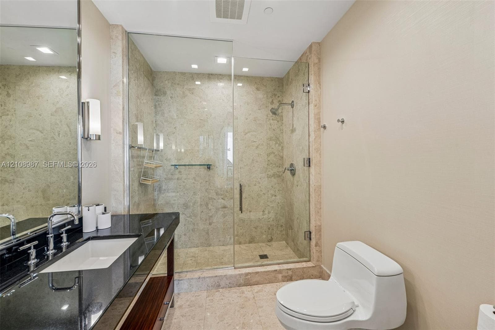Bathroom featuring a wood-finish vanity with a dark polished countertop, undermount sink, walk-in shower with stone surround and frameless glass door, and recessed lighting