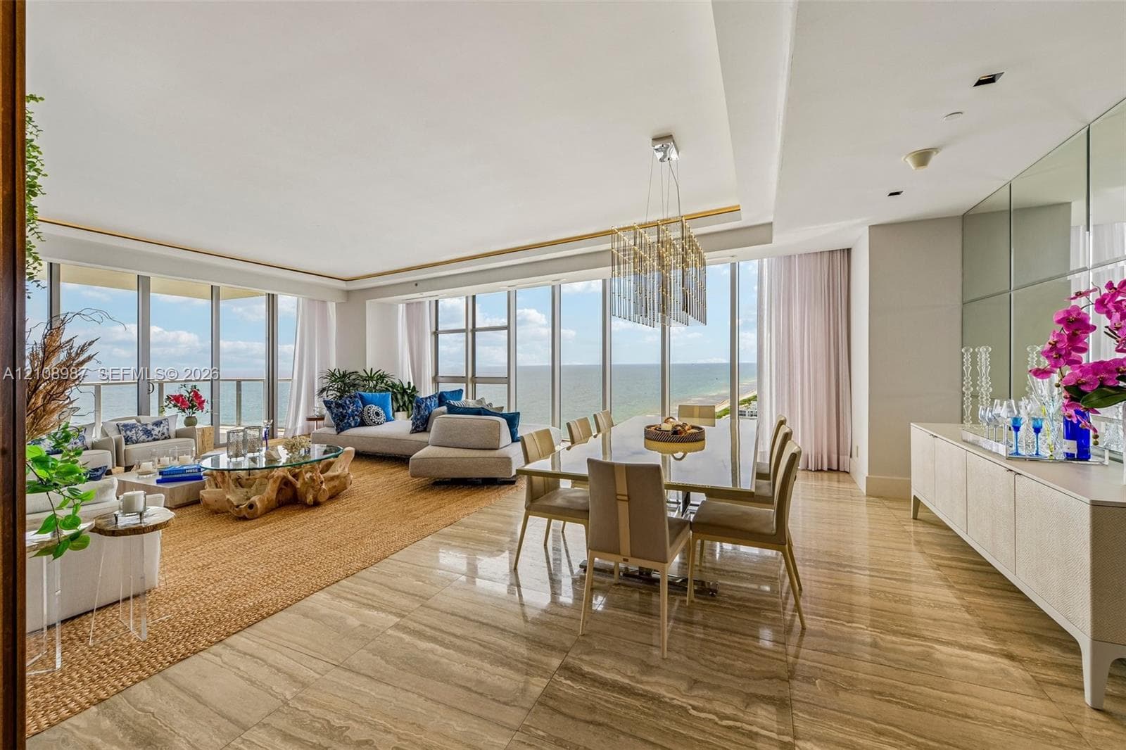 Floor-to-ceiling glass windows, stone flooring, integrated tray ceiling with recessed lighting, mirrored wall paneling, and rectangular tiered chandelier