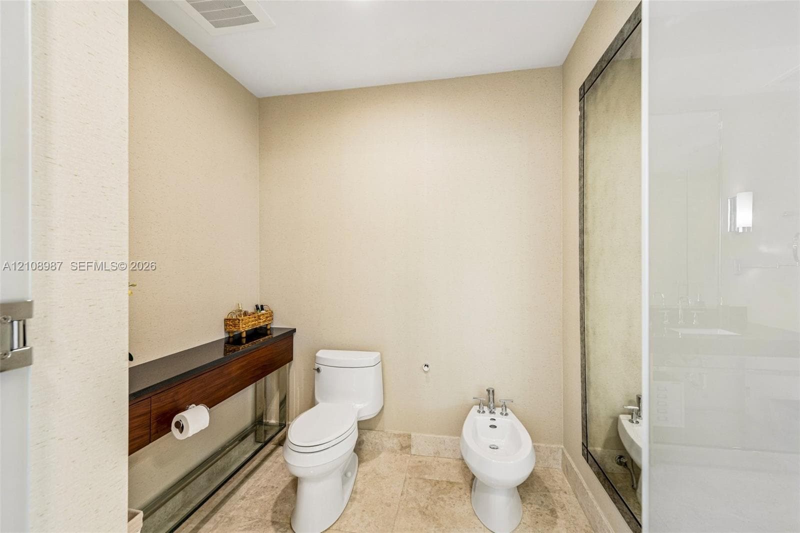Wall-mounted wood-finish vanity with a dark stone countertop, stone tile flooring, toilet, and bidet