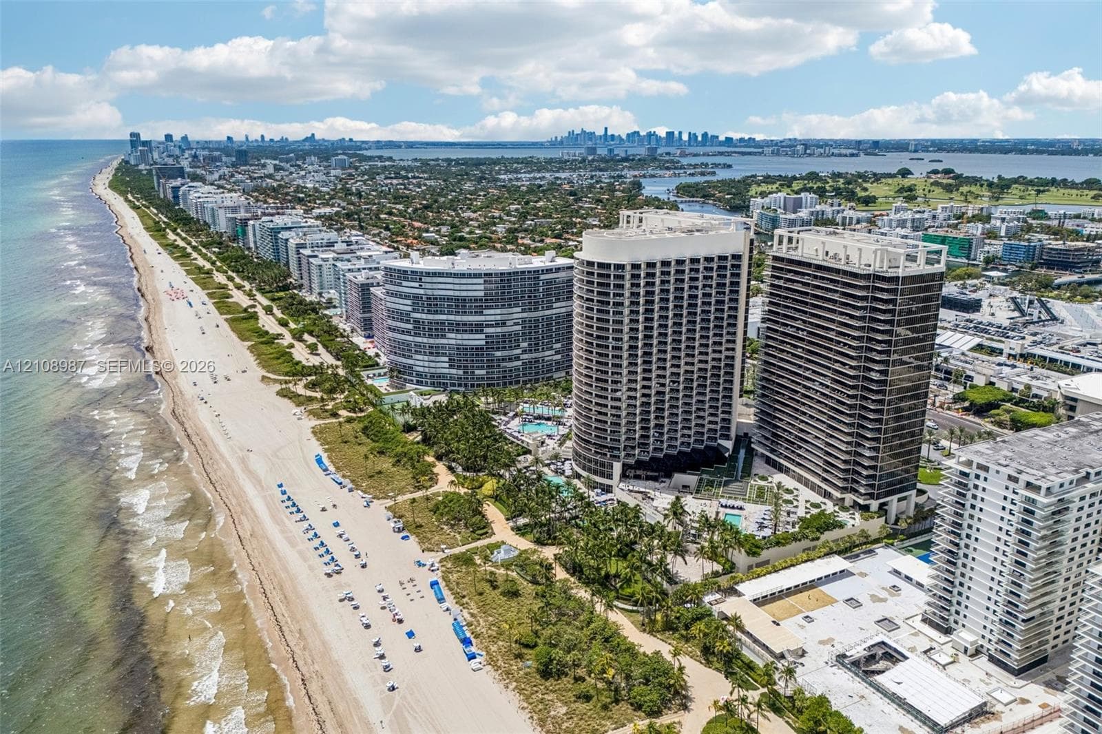 Aerial coastal perspective featuring direct beach access, high-rise residential towers, manicured palm landscaping, and expansive ocean frontage