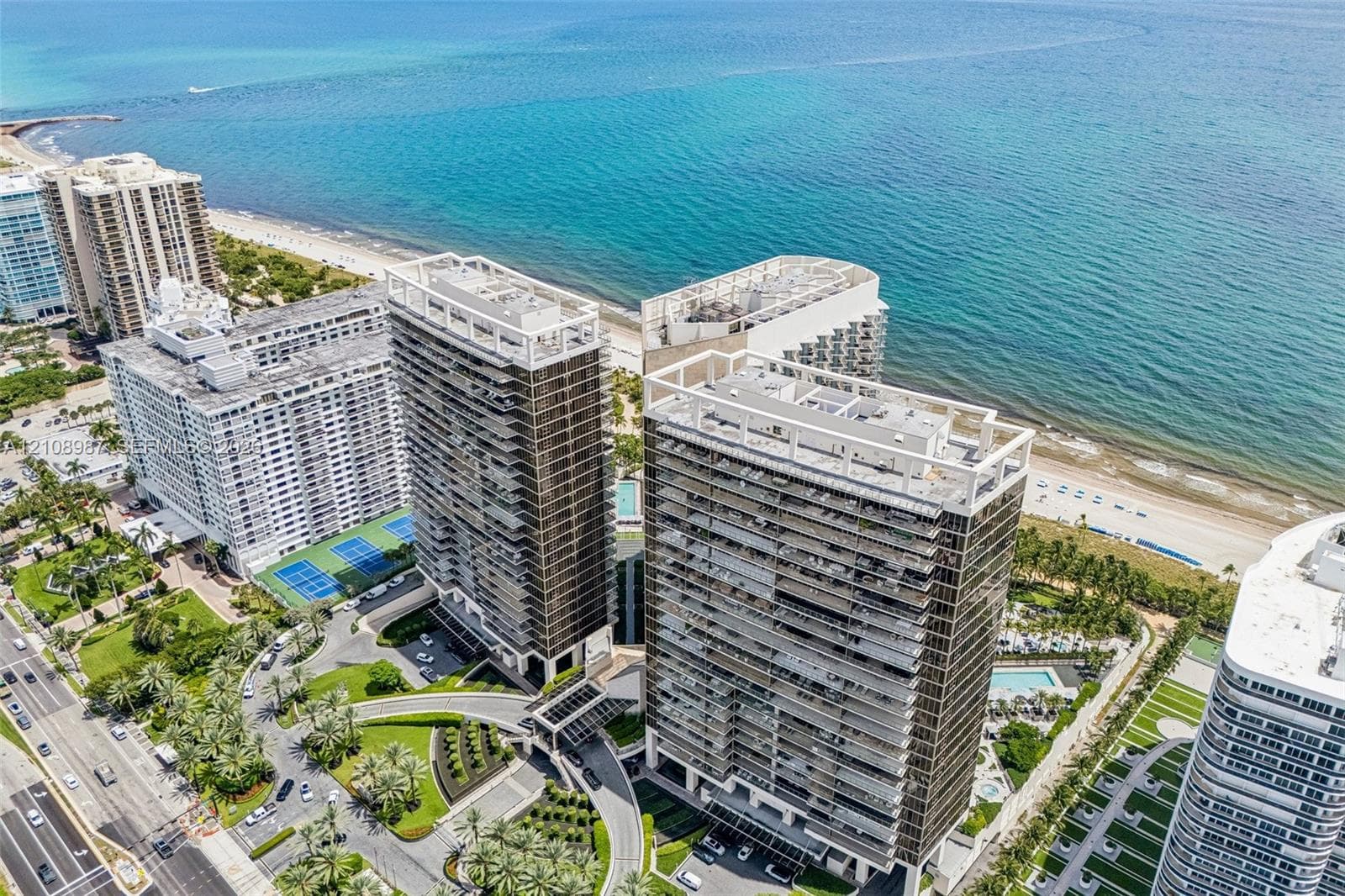 High-rise residential complex featuring private tennis courts, manicured grounds, covered porte-cochere entry, and direct proximity to the oceanfront