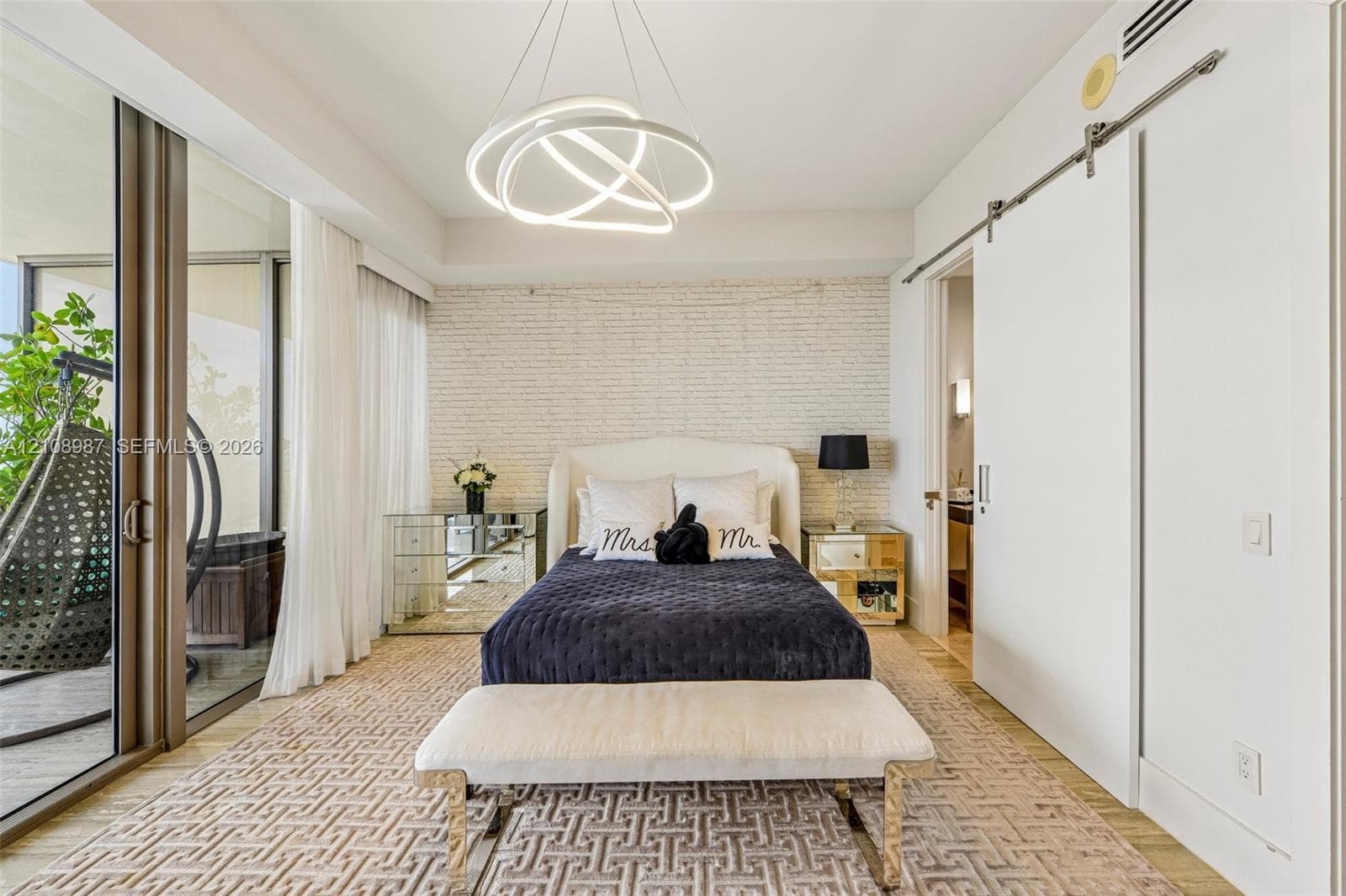 Textured brick accent wall, sculptural circular LED chandelier, floor-to-ceiling glass sliding doors, and white sliding barn door