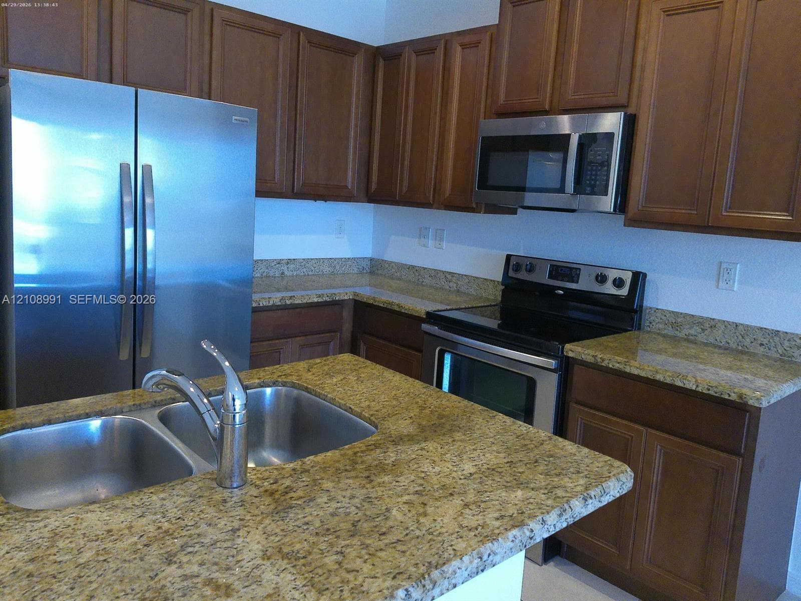 Kitchen featuring stained wood cabinetry, stone countertops, stainless steel appliances, over-the-range microwave, and dual-basin undermount sink