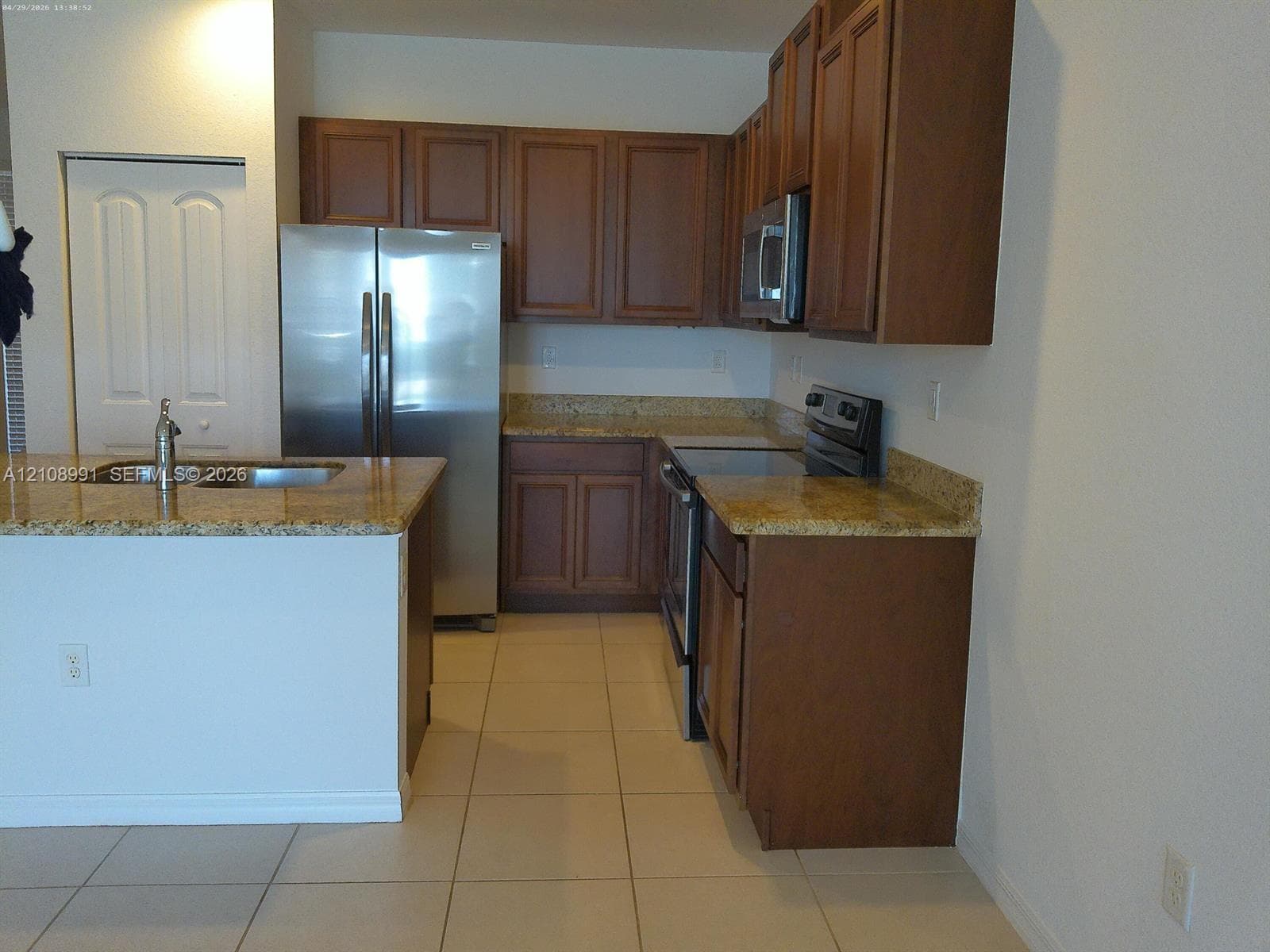 Kitchen featuring shaker-style wood cabinetry, stone-patterned countertops, stainless steel appliances, a double-basin sink, and tile flooring