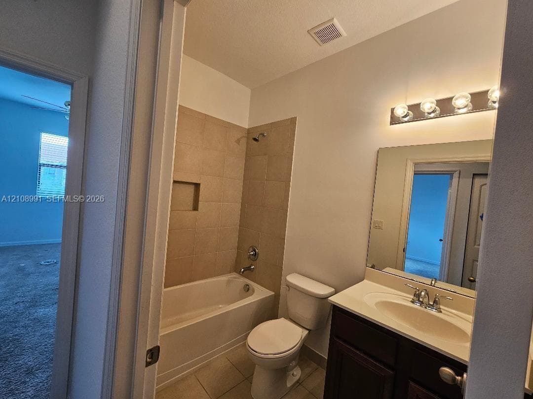 Bathroom featuring a vanity with a light-tone countertop, tub-shower combination with tile surround, built-in wall niche, and vanity mirror with multi-bulb light fixture