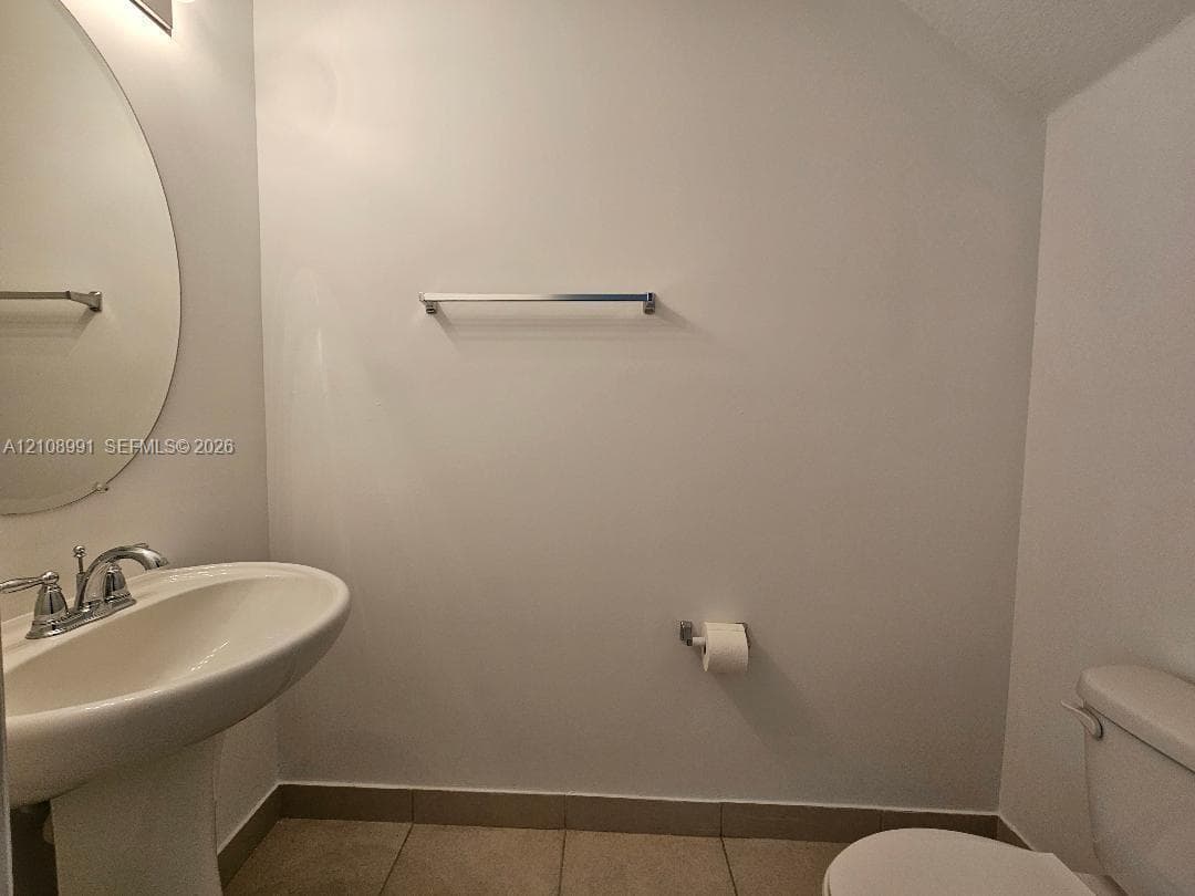 Pedestal sink with a dual-handle faucet, oval wall-mounted mirror, ceramic tile flooring, and metallic hardware fixtures
