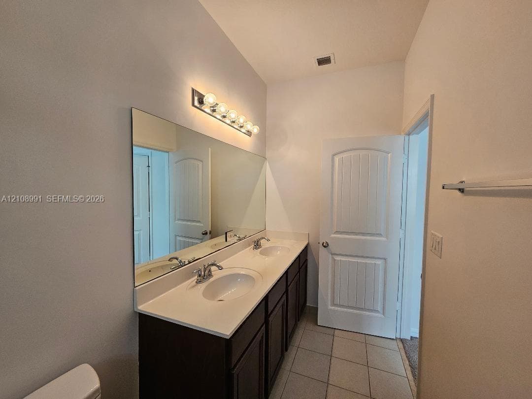 Double vanity featuring a light-toned countertop with integrated dual basins, dark-finish cabinetry, full-width wall mirror, and chrome-finish fixtures