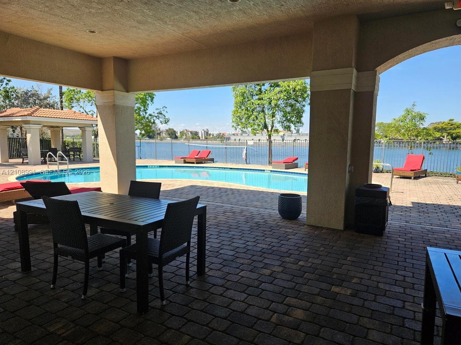 Covered brick-paver patio featuring a built-in swimming pool, detached gazebo, and metal fencing along the water