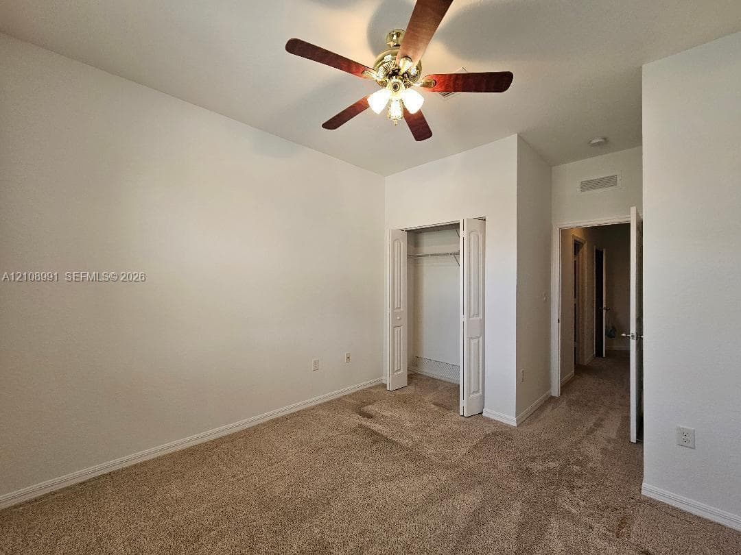 Neutral wall tones, carpeted flooring, built-in closet with folding doors, and a ceiling-mounted light fixture with a fan
