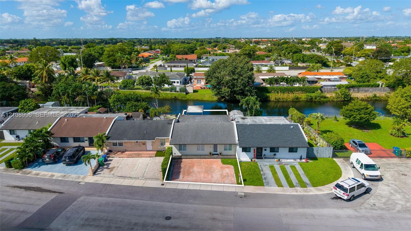 Aerial perspective of a single-story residence featuring a shingled roof, a paved front courtyard, and direct canal frontage with a manicured rear lawn